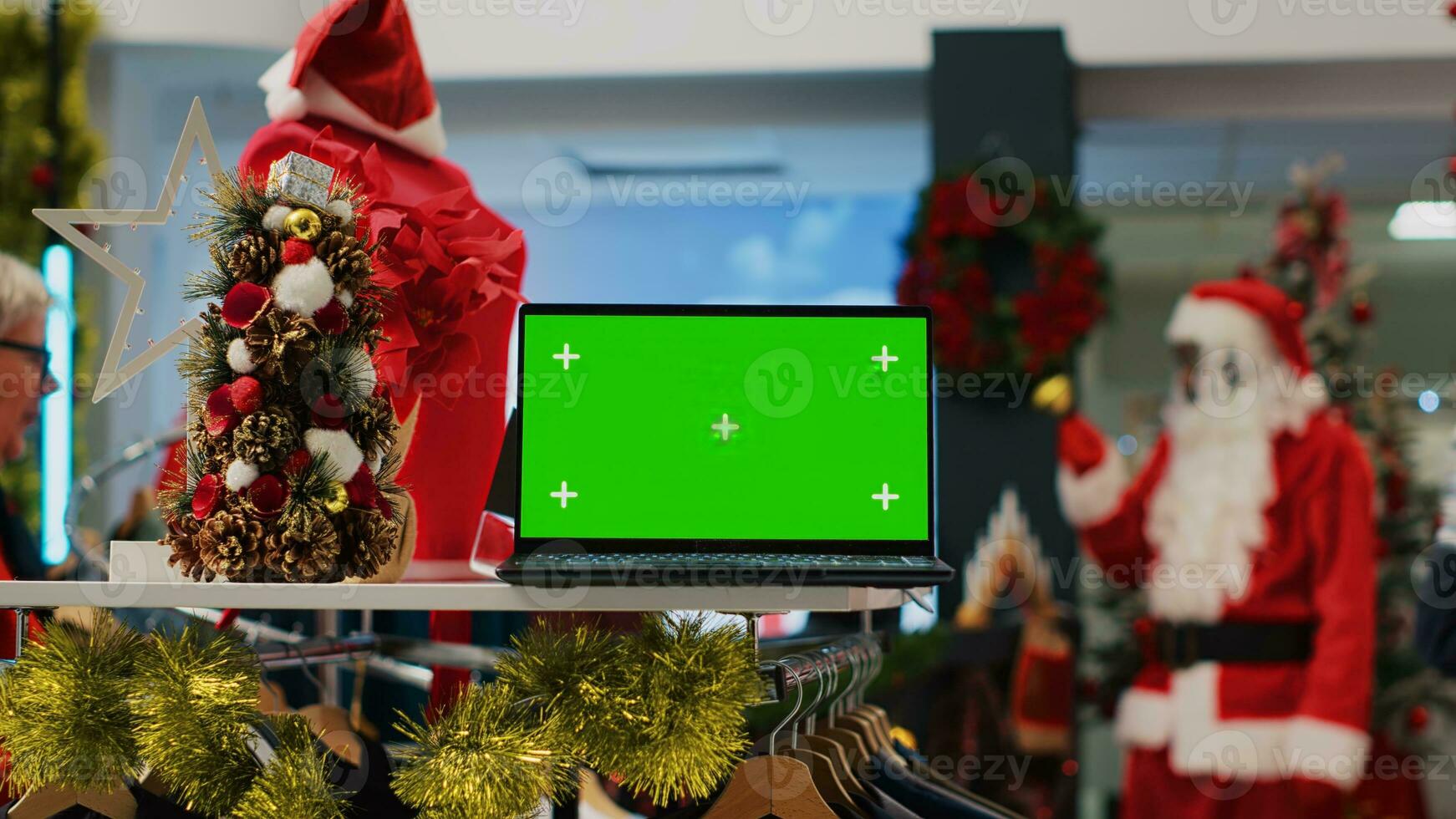 Mockup laptop on xmas decorated clothing store display table showing information about products. Green screen device in shopping mall fashion shop useful for looking up clothes prices photo