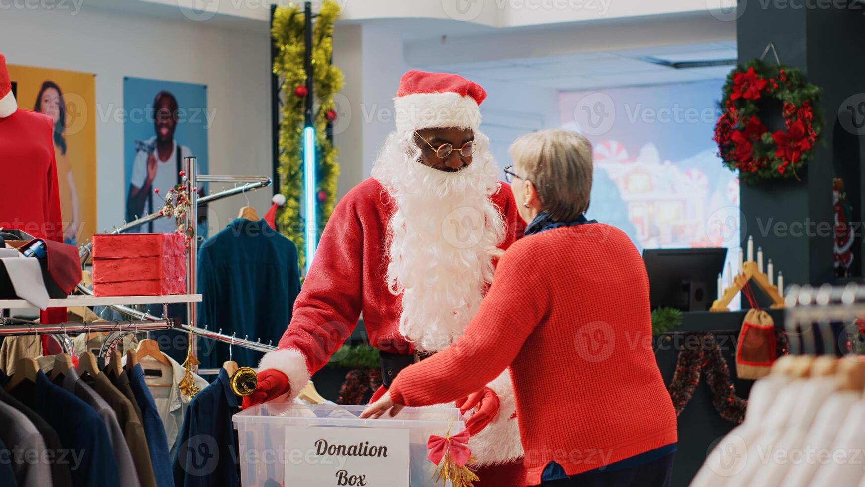 Retail assistant dressed as Santa Claus collecting unneeded clothes from clients in donation box, giving them as present to those in need during Christmas season, spreading holiday cheer photo