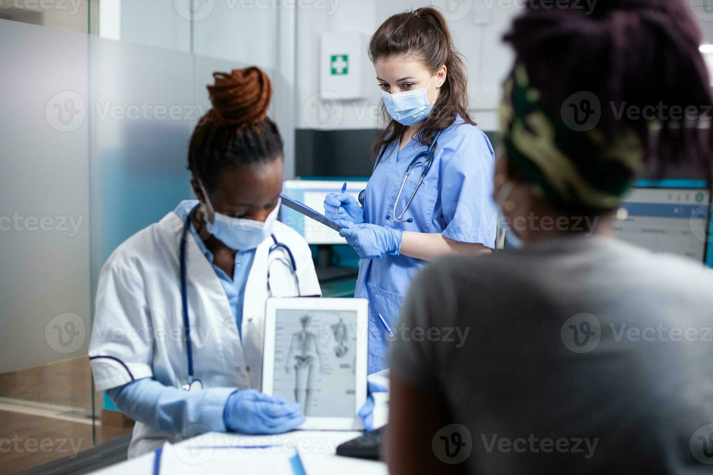 Orthopedic doctor at physical consultation offering informations to patient on tablet using human skeleton figure. Bone specialist providing healthcare diagnosis to woman at appointment checkup photo