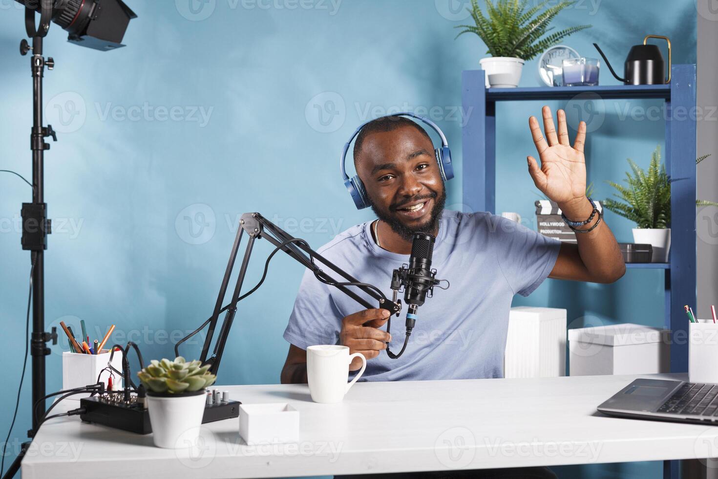 Smiling streamer wearing headphones greeting audience while creating digital content and looking at camera. Cheerful influencer in headset recording video for internet blog photo