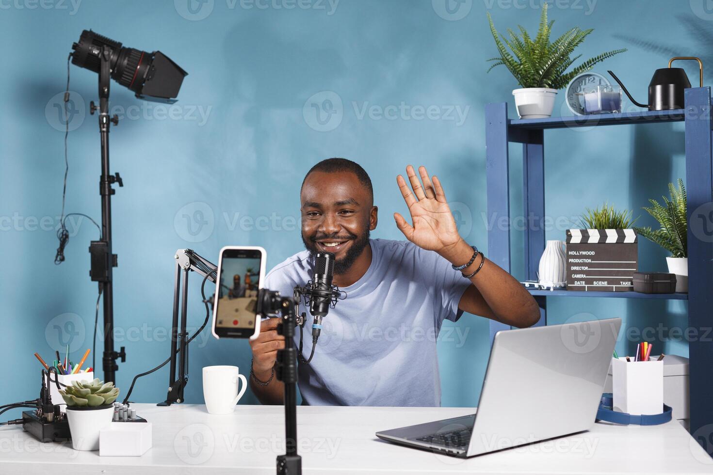 Cheerful blogger creating web content and live streaming using smartphone. Smiling vlogger greeting subscribers and looking at mobile phone camera while recording video for internet channel photo