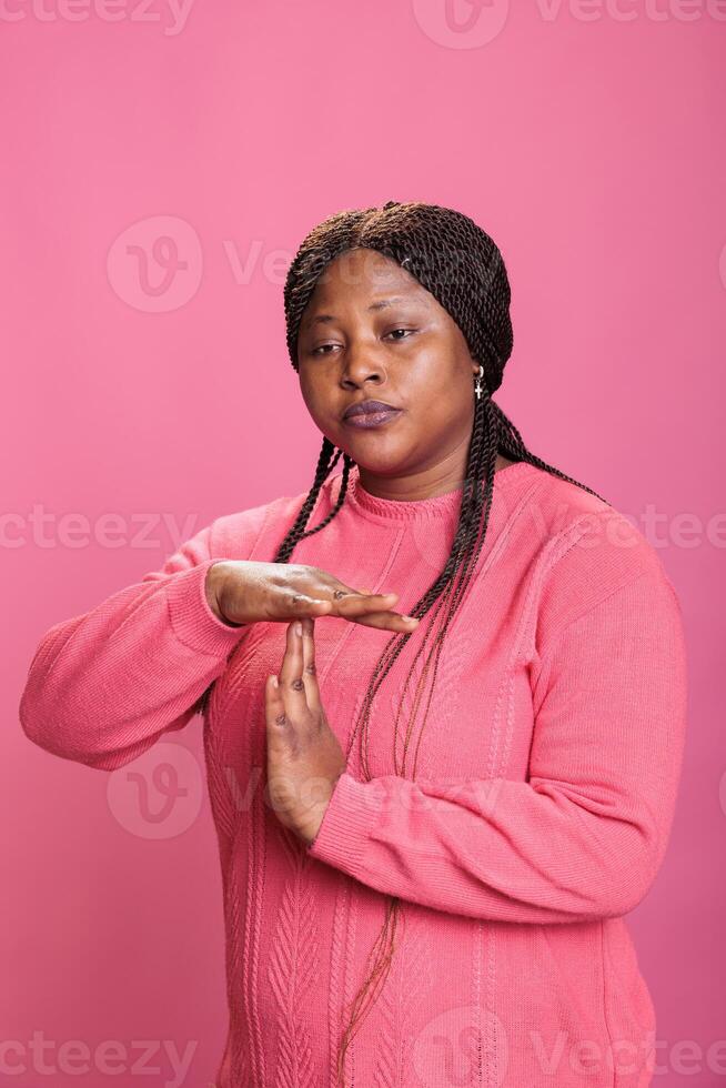 Disapproval negative woman doing timeout and break gesture while making displeased expression in studio, holding handd in t shape sign. Serious young woman advertising refuse in studio photo