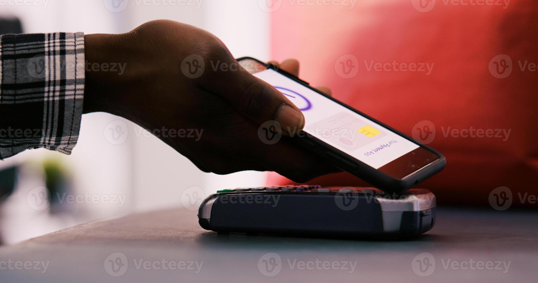 African american shopper putting phone on pos terminal after buying stylish merchandise and accessories in clothing store. Customer paying for fashionable casual wear at counter desk. Close up. photo