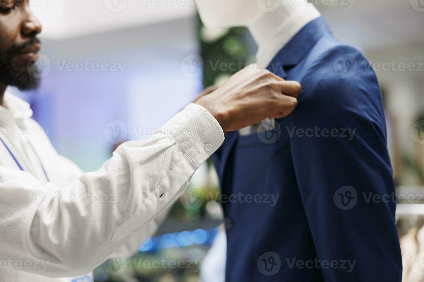 Clothing store assistant hands fastening jacket on mannequin to showcase new collection for customers. Fashion boutique african american employee dressing dummy model to display apparel in shop photo