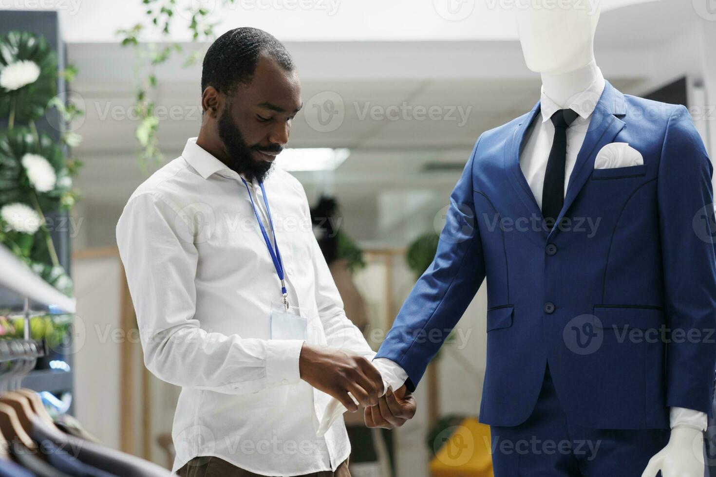 compras centro comercial trabajador vendaje maniquí en formal masculino traje, fijación botones en camisa manga. ropa Tienda africano americano hombre asistente creando elegante atuendo en Moda sala de exposición foto