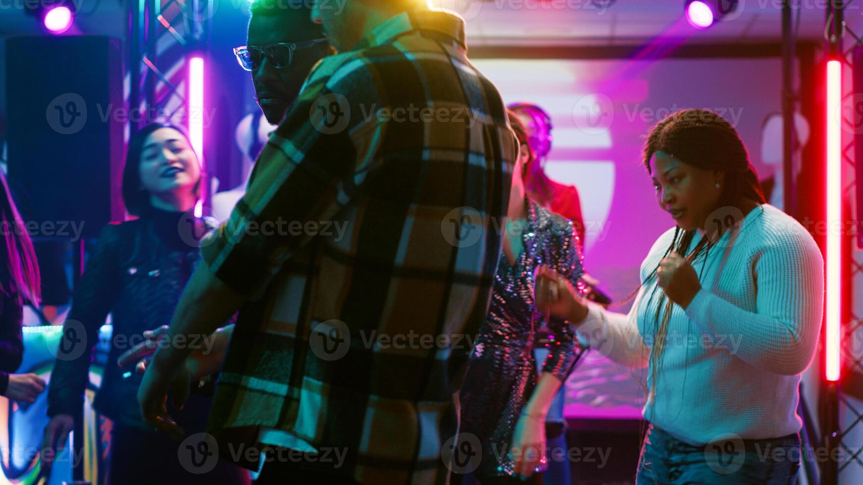 Multiethnic group of people dancing, feeling funky on music at the club. Friends enjoying live performance on dance floor, showing dance moves under disco lights and partying. Tripod shot. photo