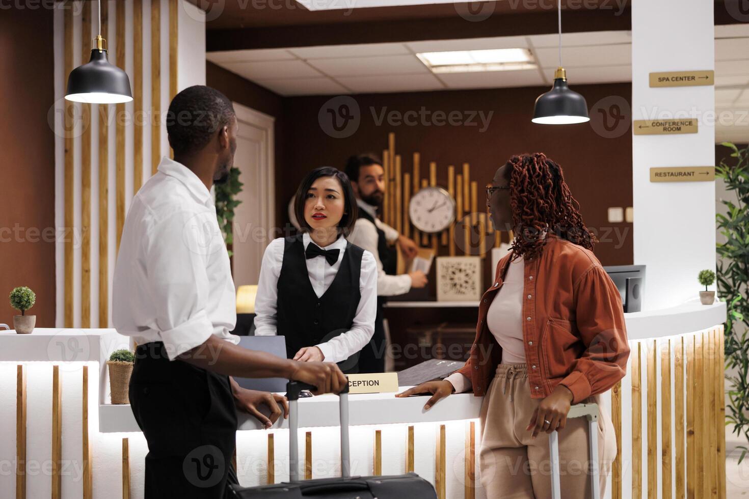 Hotel employee registering people at front desk, using computer to review room reservation and booking details. Receptionist welcoming guests in luxury resort, check in register. photo
