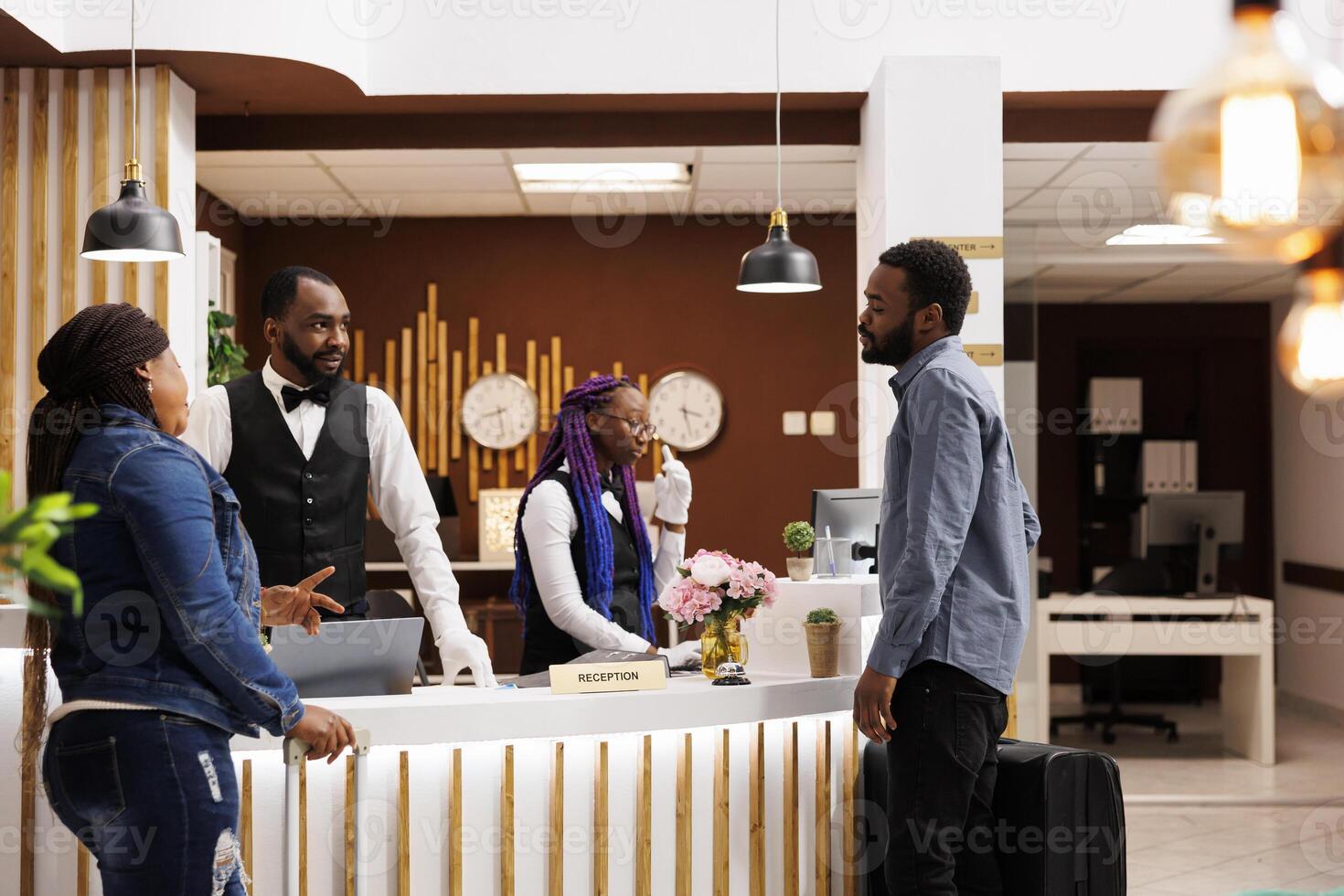 Tired unhappy people tourists standing at front desk waiting for checkin procedure, feeling exhausted sleepy after long flight. African American couple arrive at luxury resort wait for room be ready photo