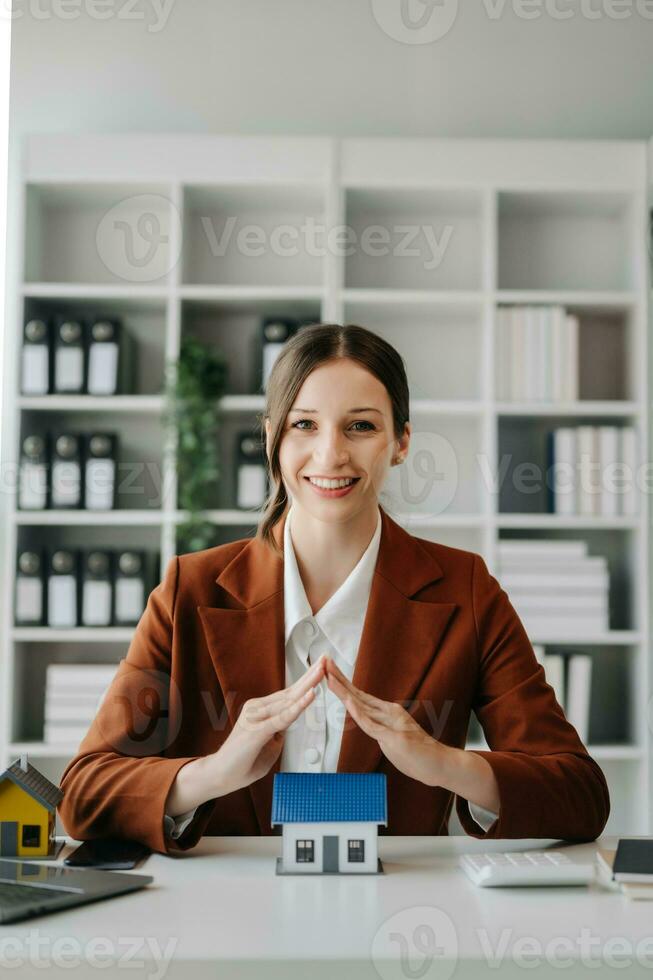 Female real estate agent is use hands to protect red roof for the concept of real estate investment about house trading, purchase at desk in office photo
