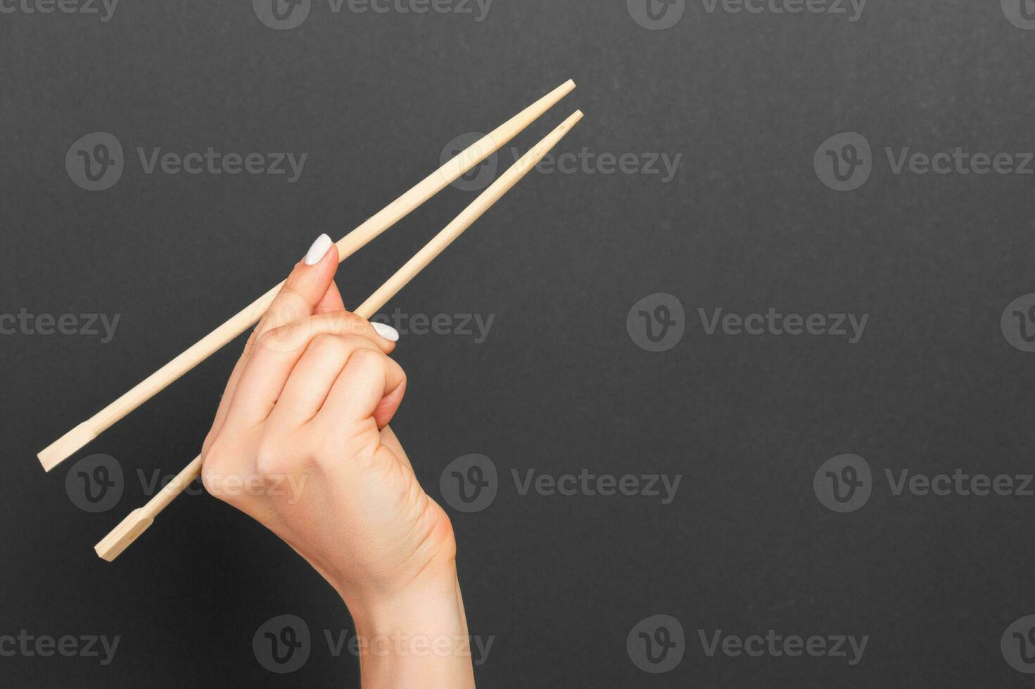 Creative image of wooden chopsticks in female hand on black background. Japanese and chinese food with copy space photo