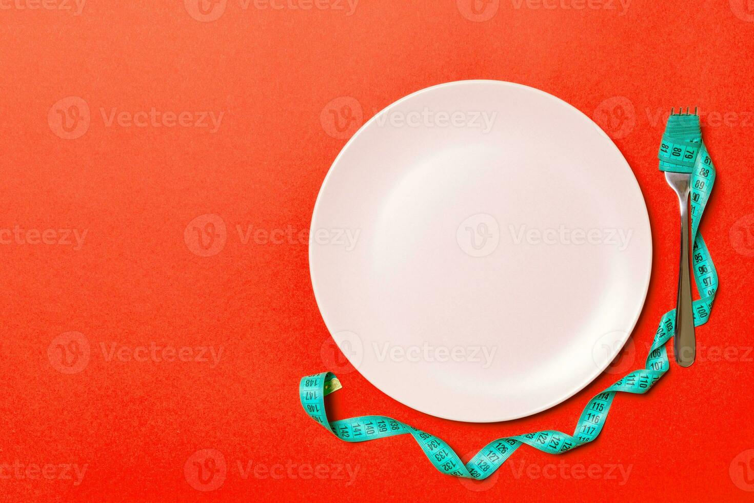 Top view of fork with measure tape near round plate on red background. Weight loss concept with empty space for your idea photo