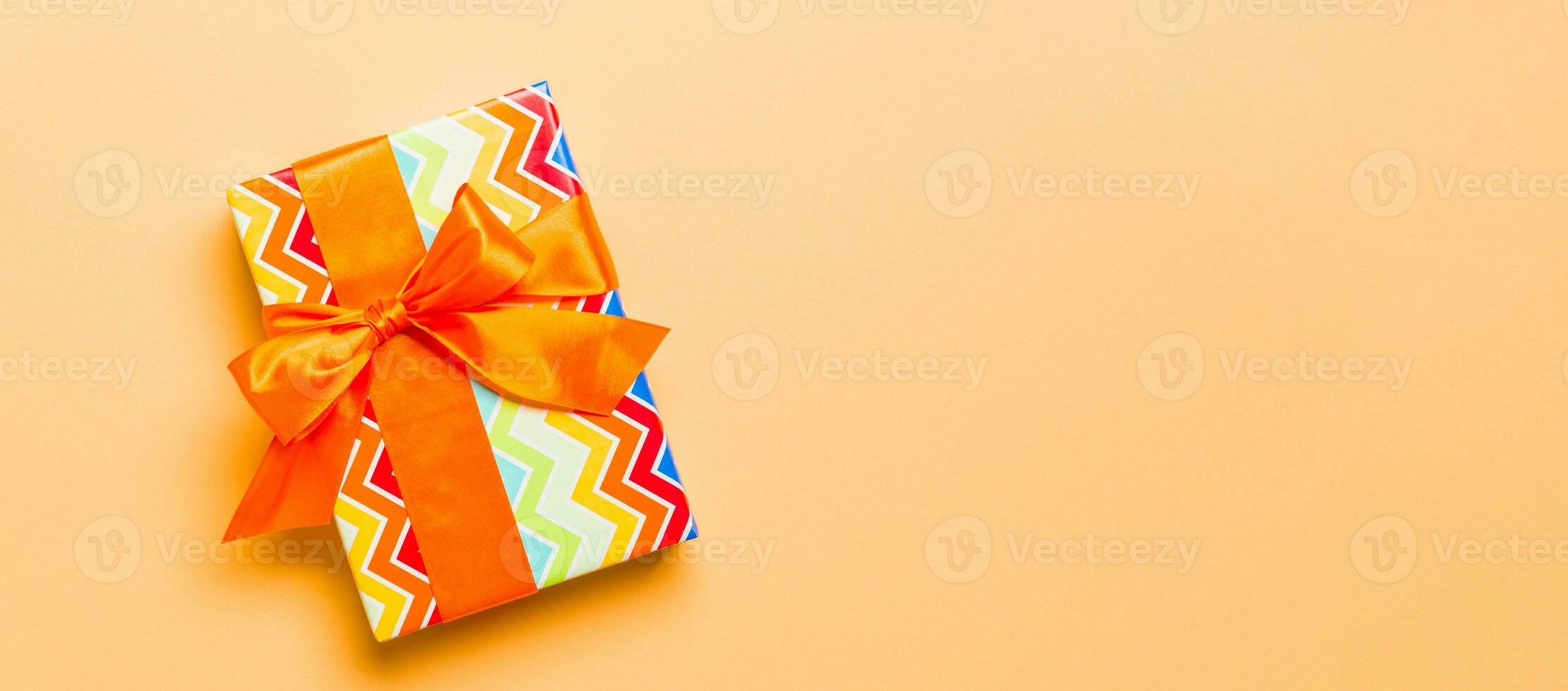 wrapped Christmas or other holiday handmade present in paper with orange ribbon on orange background. Present box, decoration of gift on colored table, top view with copy space photo