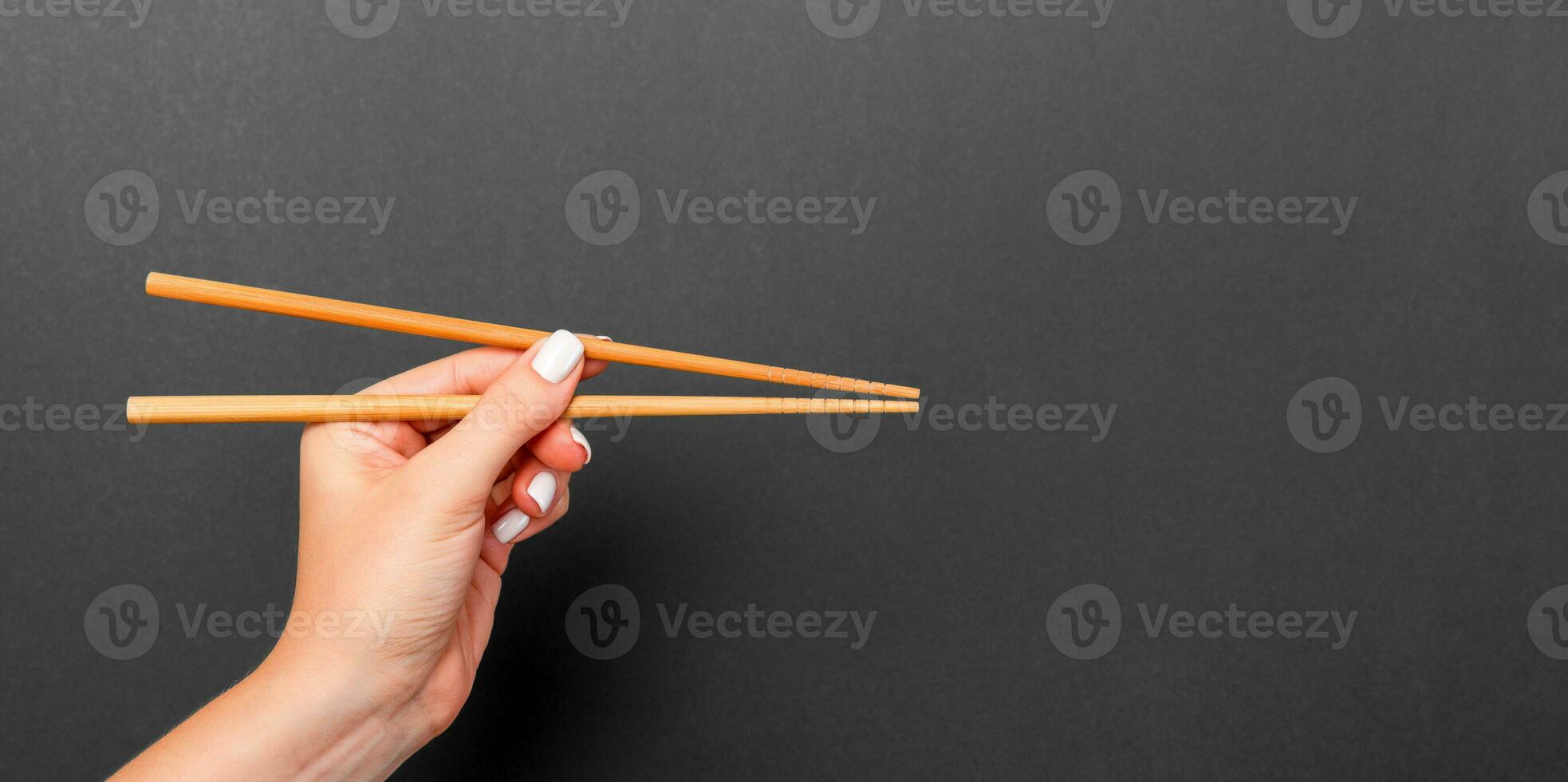 Wooden chopsticks in female hand on black background with empty space for your idea. Tasty food concept photo