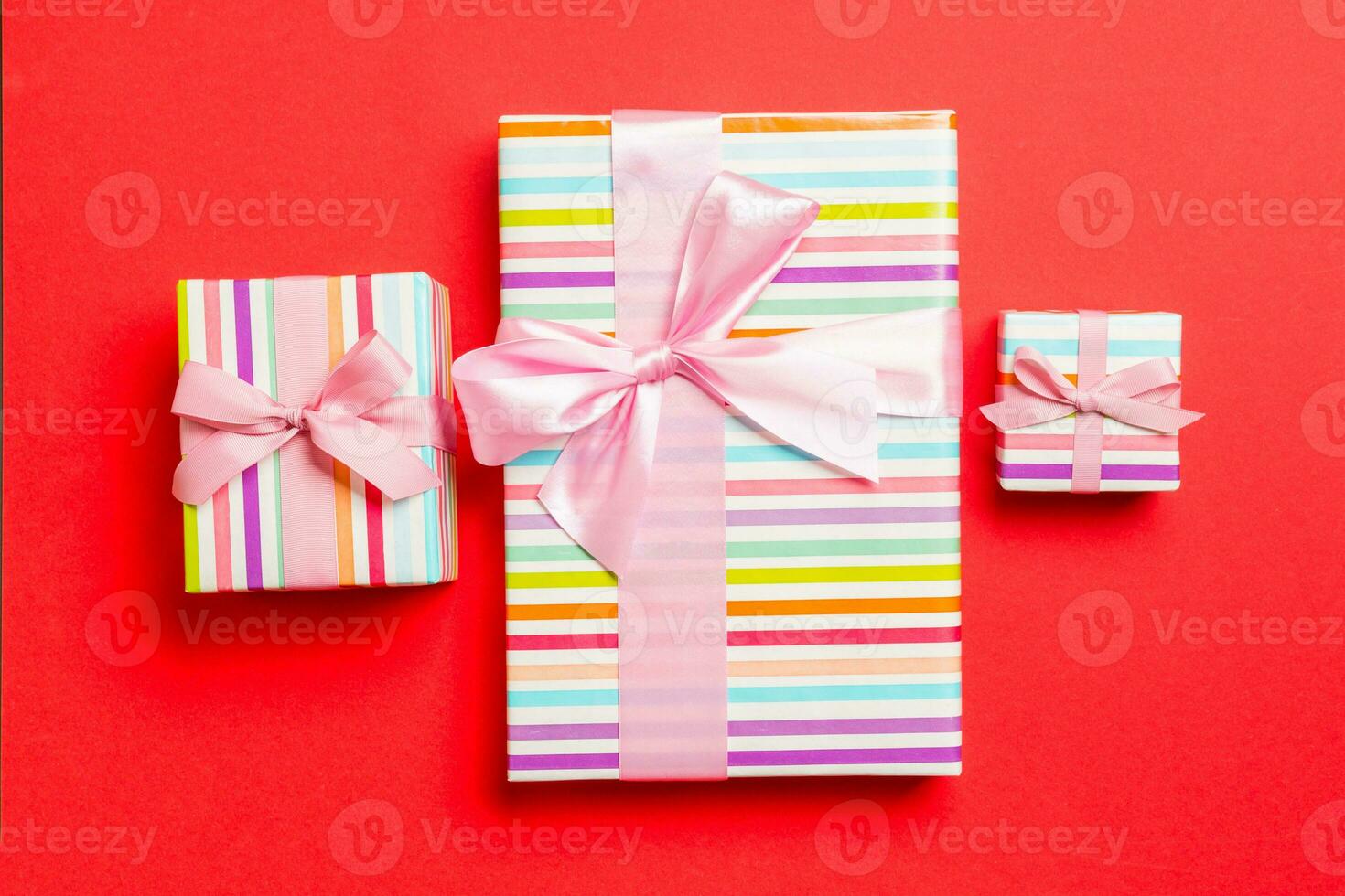 wrapped Christmas or other holiday handmade present in paper with pink ribbon on red background. Present box, decoration of gift on colored table, top view photo