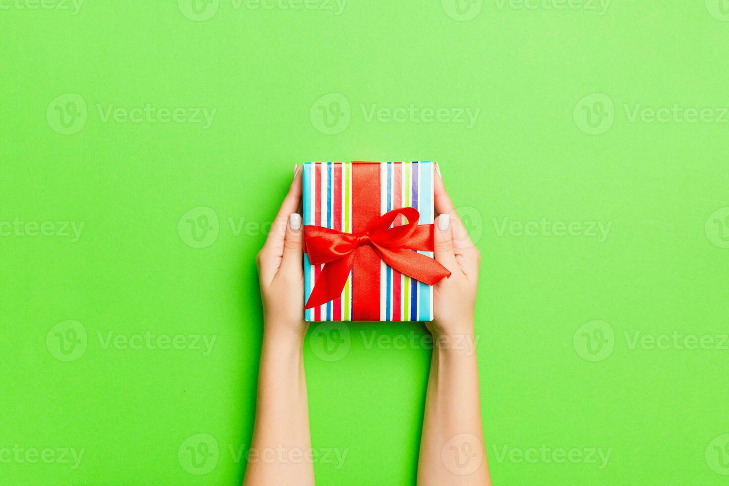 Top view of female hands holding christmas or other holiday handmade present box package in the palms, flat lay table background with copy space photo