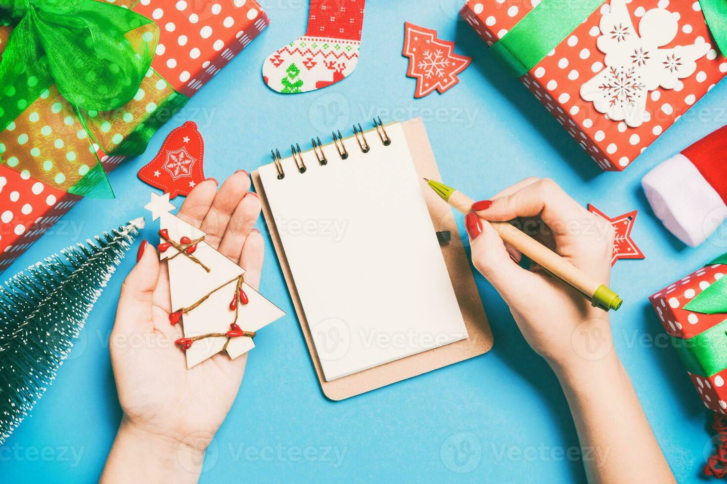 Top view of female hand making some notes in noteebok on blue background. New Year decorations and toys. Christmas time concept photo
