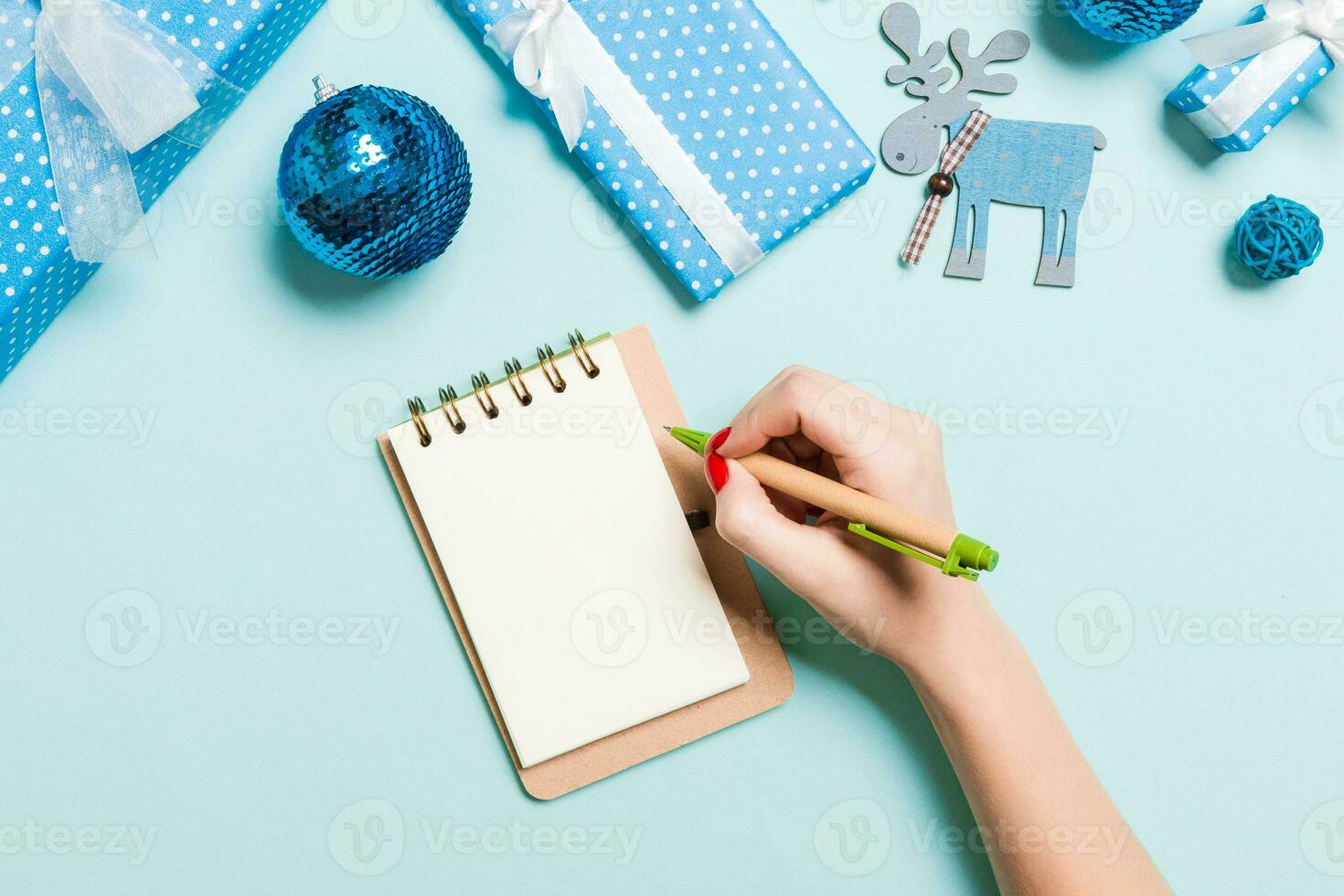 Top view of female hand making some notes in noteebok on blue background. New Year decorations and toys. Christmas time concept photo