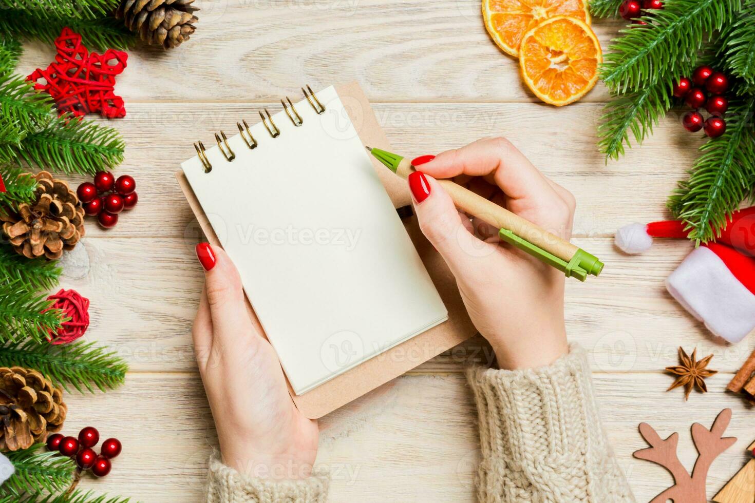 Top view of female hand writing in a notebook on wooden Christmas background. Fir tree and festive decorations. Wish list. New Year concept photo