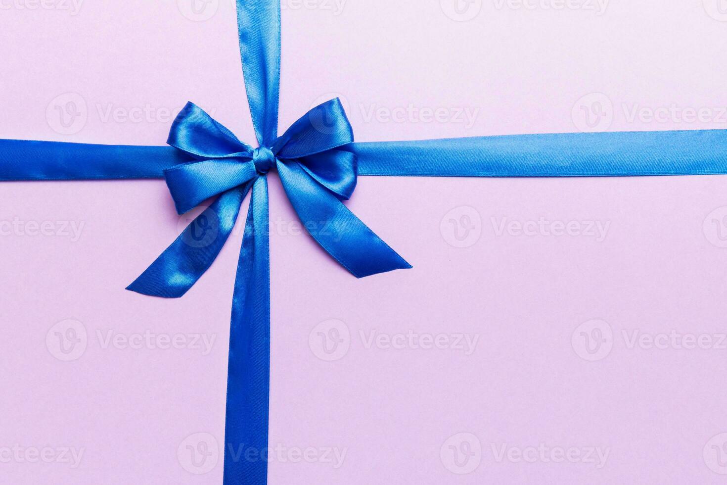 Top view of blue ribbon rolled and blue bow isolated on colored background. Flat lay with copy space photo