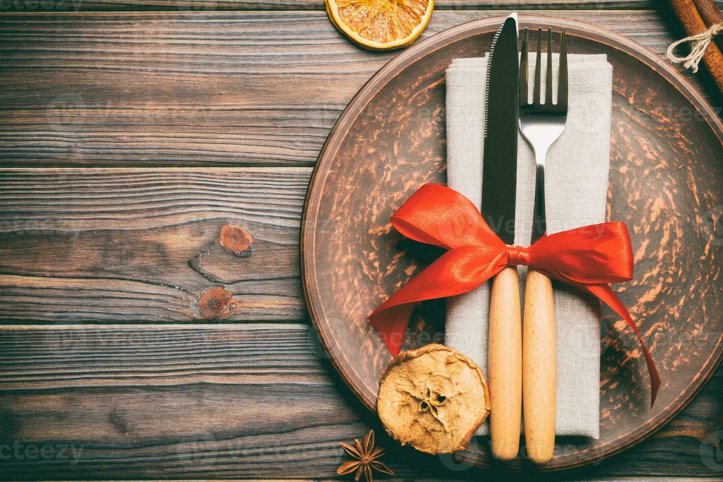 Top view of holiday dinner decorated with dried fruit and cinnamon on wooden background. Set of plate, urensil and New Year decorations. Christmas time concept with epmty space for your design photo