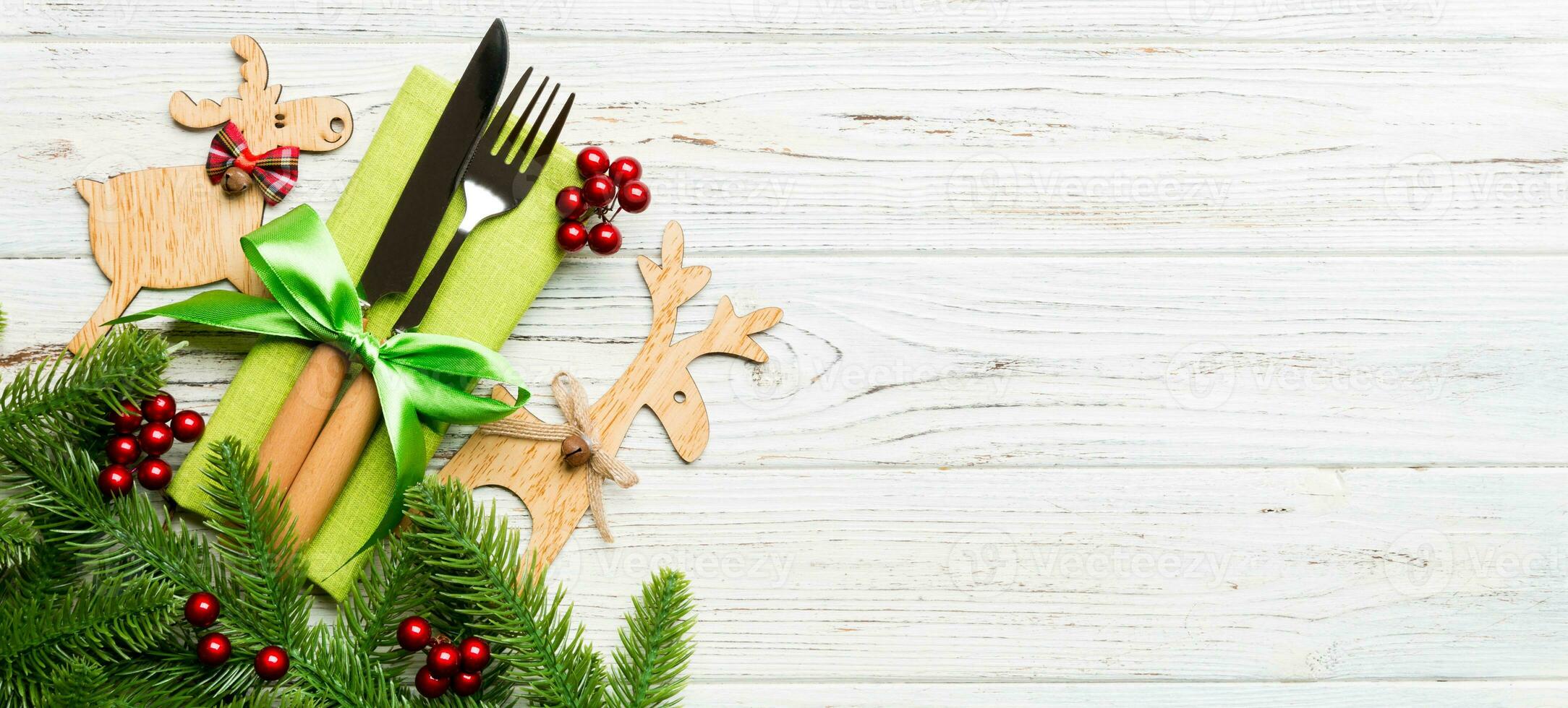 Banner top view of holiday objects on wooden background. Utensils tied up with ribbon on napkin. Christmas decorations and reindeer with copy space. New year dinner concept photo