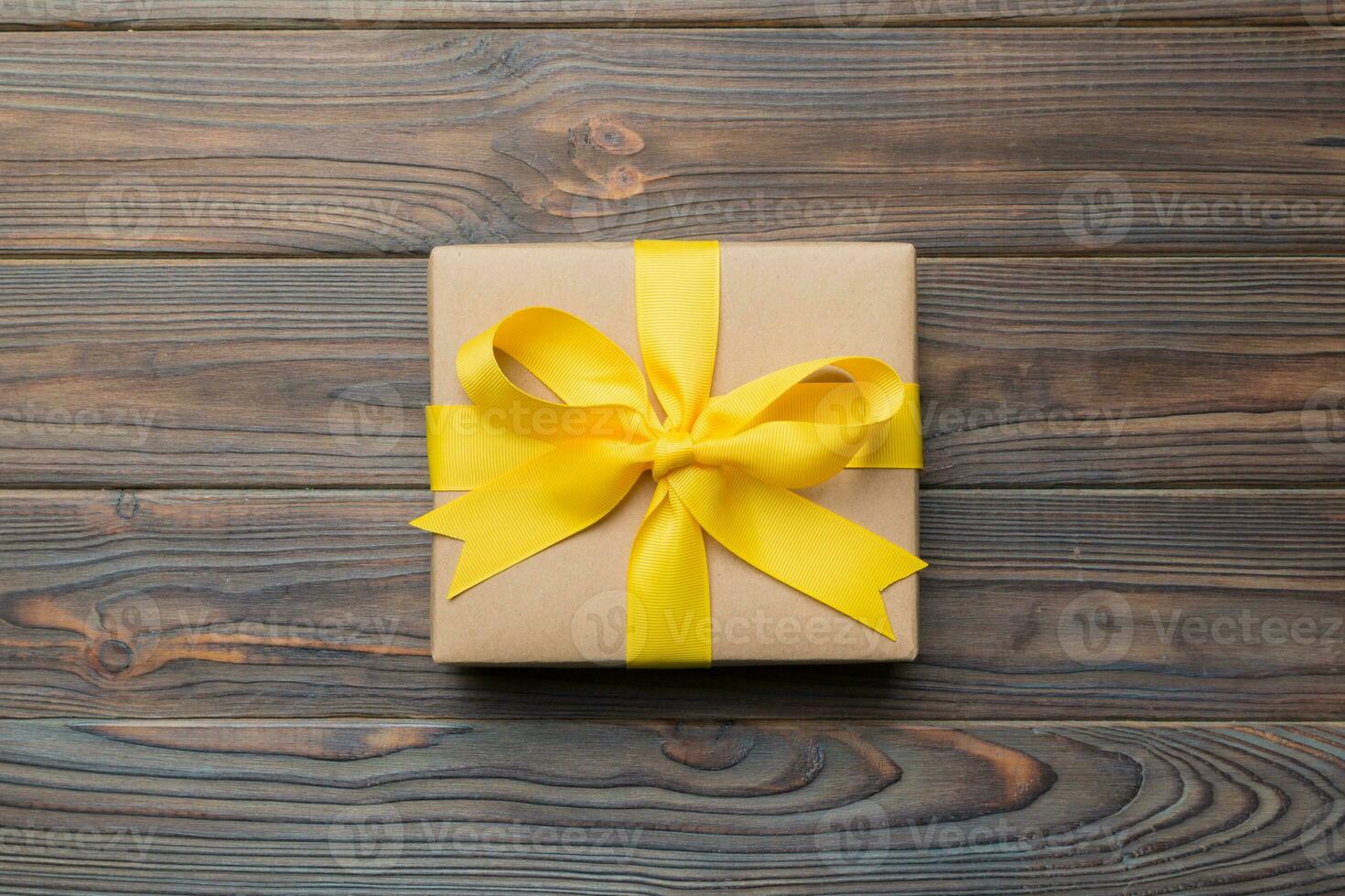 Holiday gift box wrapped in craft paper with colored bow on table background. Top view, flat lay, copy space photo