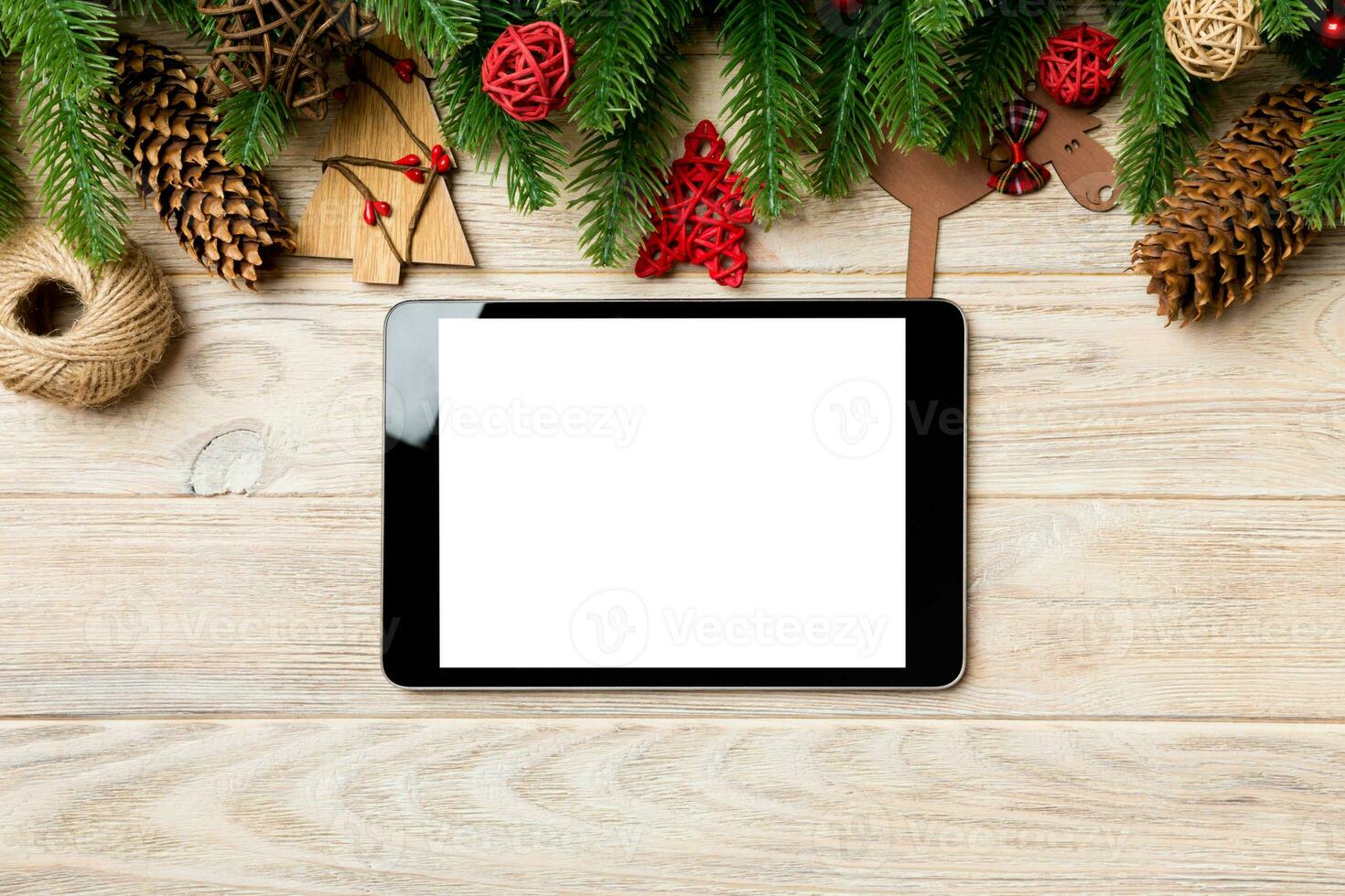 Top view of tablet, Christmas toys, decorations and fir tree branches on wooden background. New Year holiday concept with copy space photo