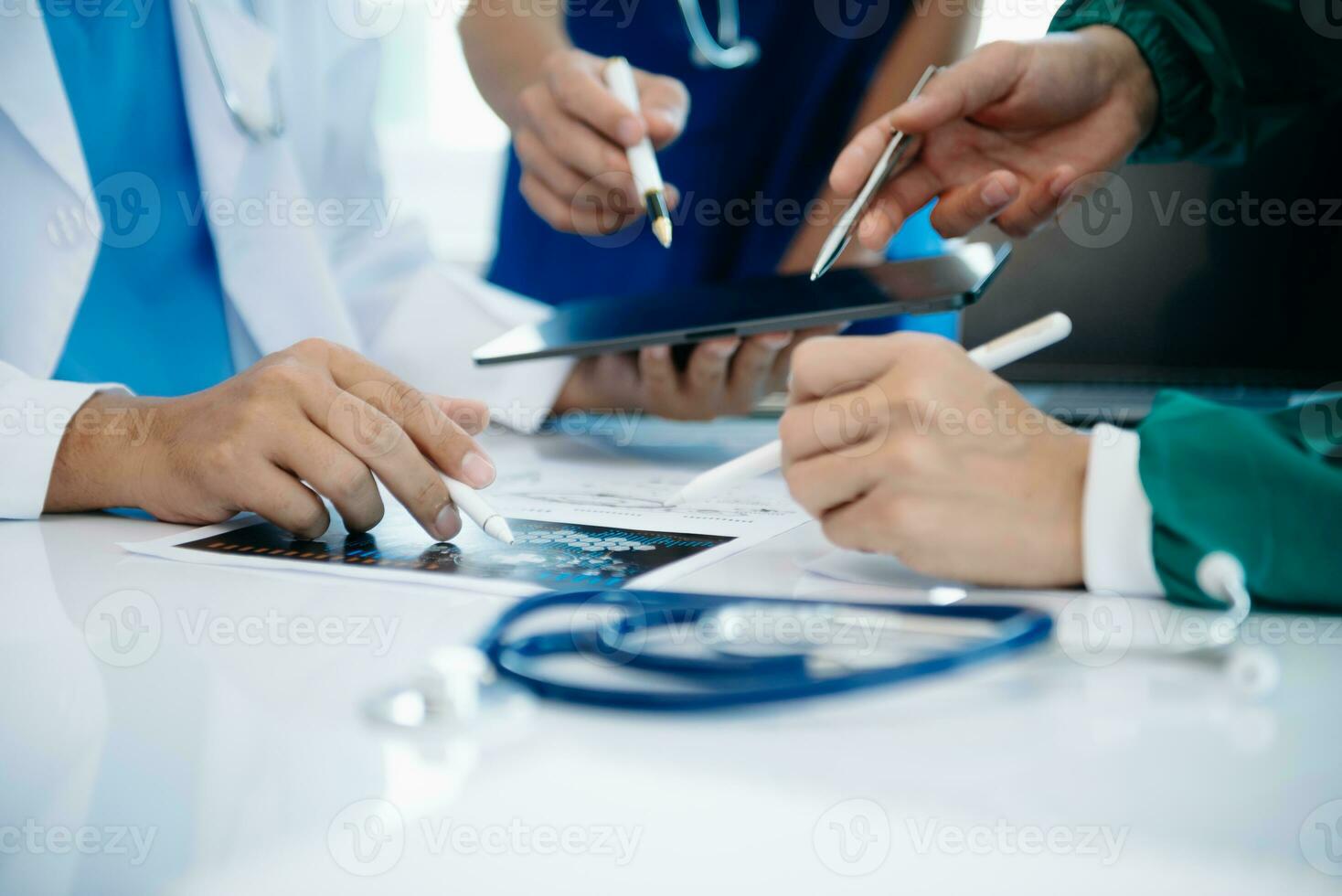 Medical team having a meeting with doctors in white lab coats and surgical scrubs seated at a table discussing a patients working online using computers photo