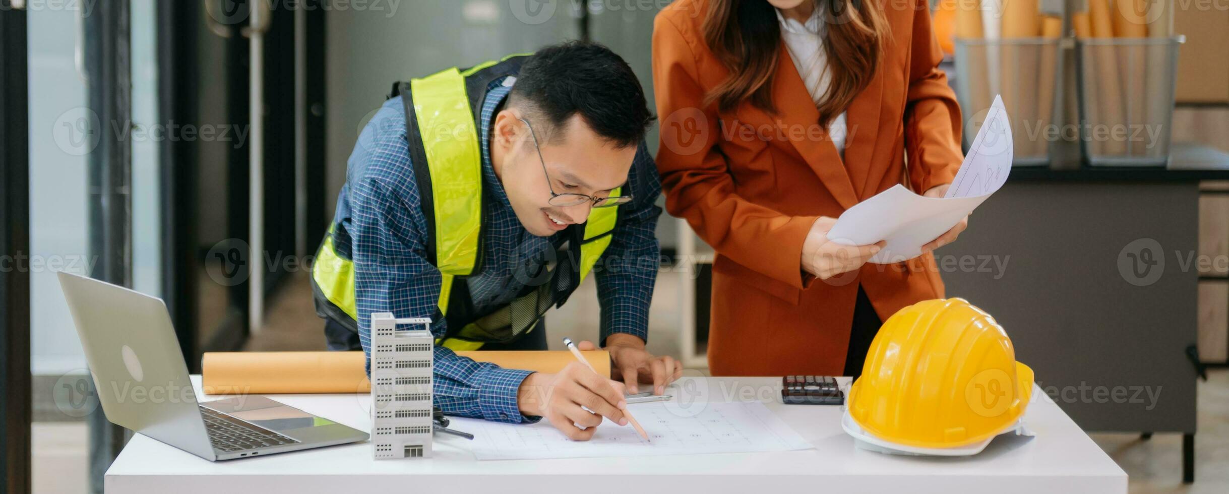 dos colegas que se discute datos trabajando y tableta, ordenador portátil con en arquitectónico proyecto a construcción sitio a escritorio en oficina foto