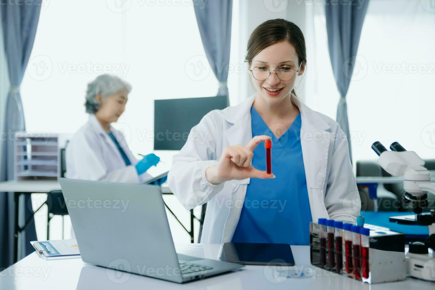 Confident young Caucasian female doctor in white medical uniform sit at desk working on computer. Smiling use laptop write in medical journal in clinic. photo