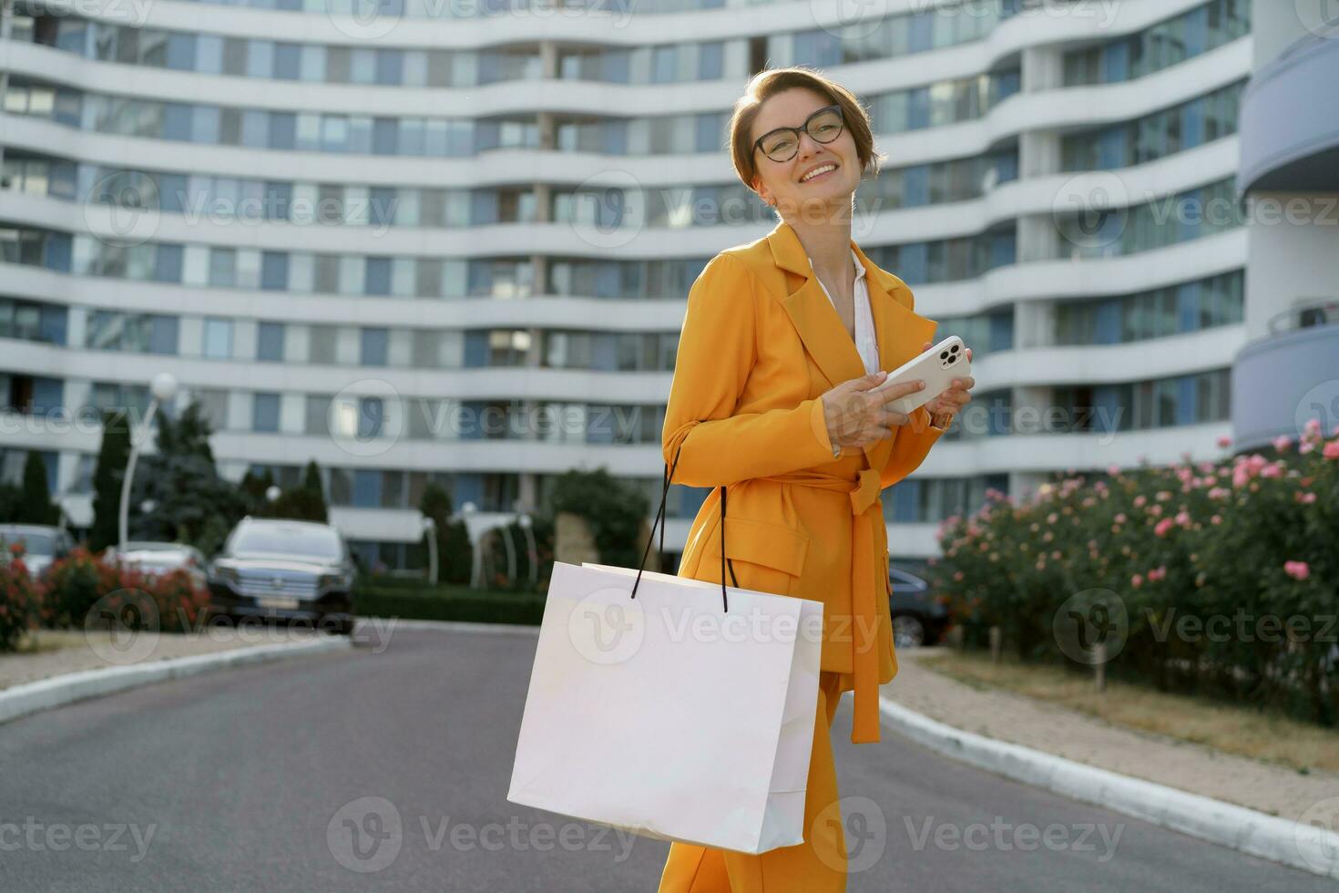 Stylish brunette  woman with short haircut holding shopping bag , walking outdoor over modern building. photo