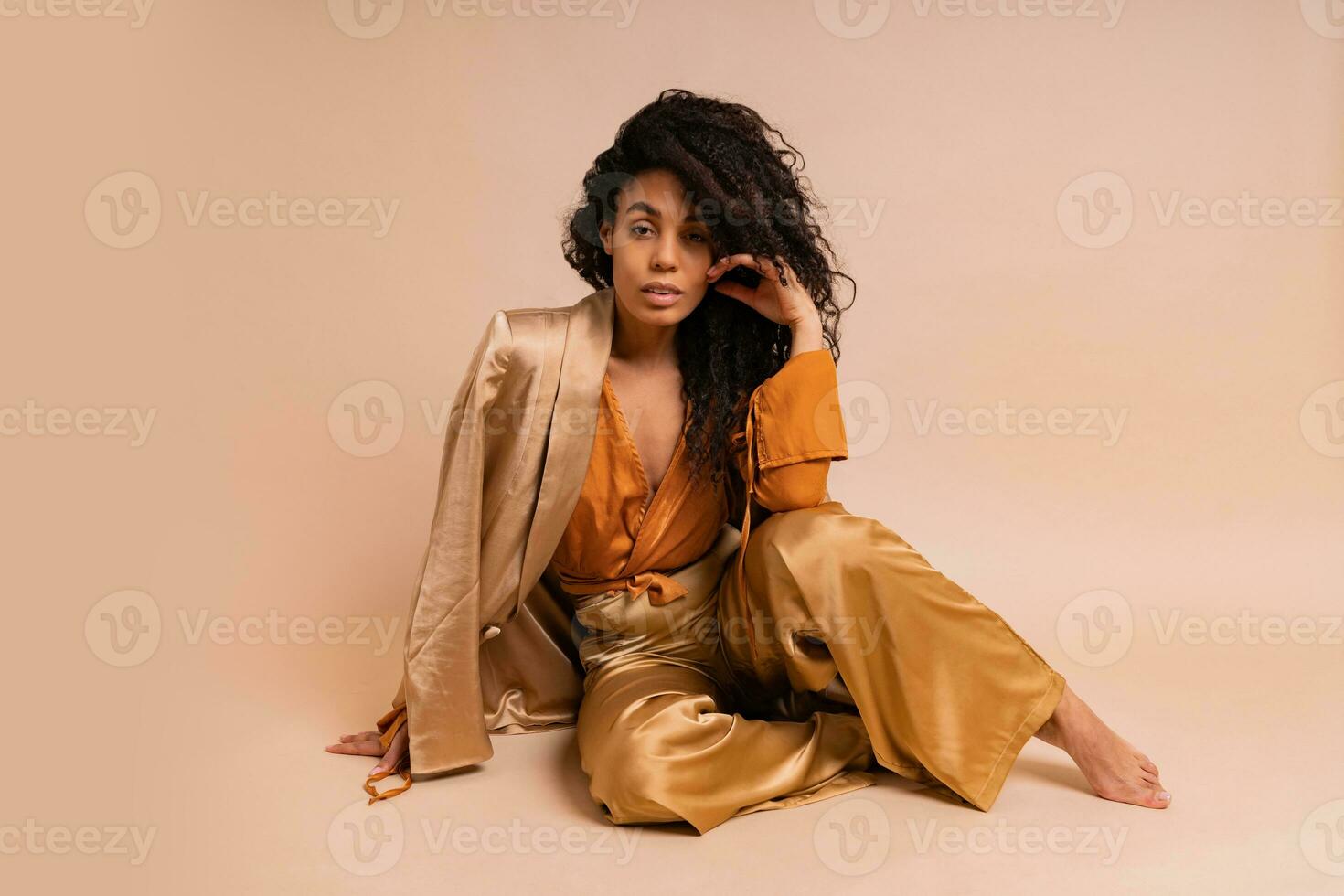Stunning  african model with voluminous curly hairstyle in elegant   costume posing in studio on beige background. photo