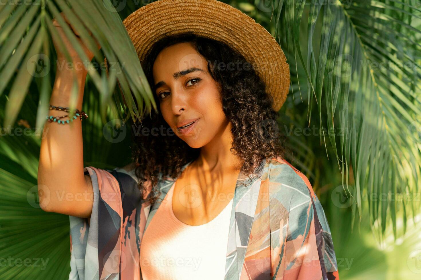 cerca arriba retrato de hermosa mujer en Paja sombrero y verano elegante atuendo posando en tropical jardín. foto