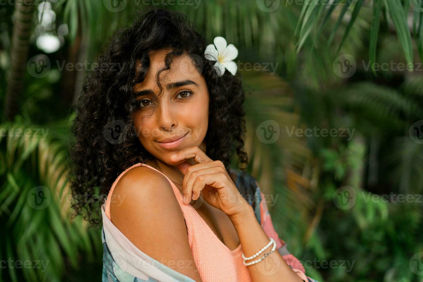 cerca arriba retrato de feliz mujer con plumeria flor en pelos después spa en lujo complejo. vistiendo boho tropical atuendo. foto