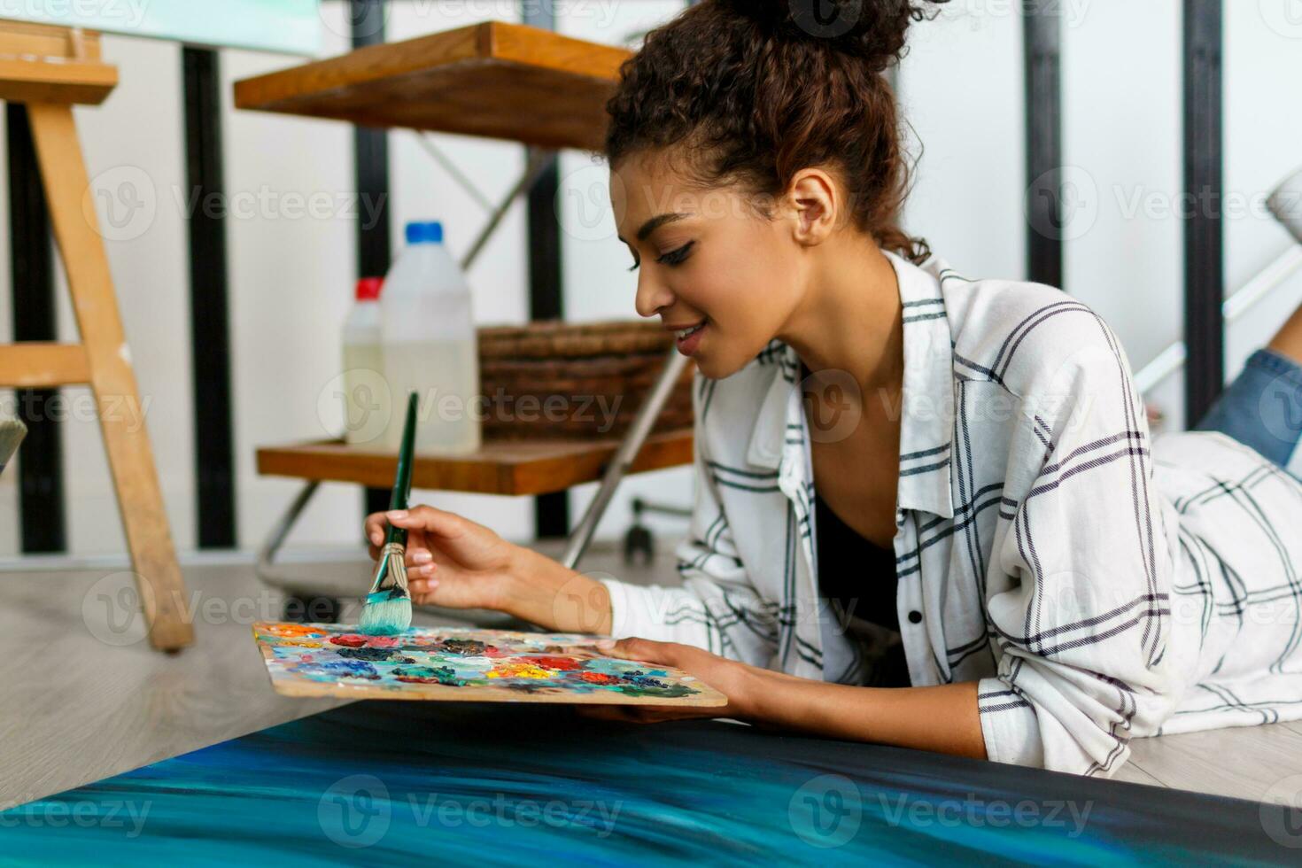 Woman painter lies on the floor  near  canvas and drawing. Artist studio interior. Drawing supplies, oil paints, artist brushes, canvas, frame.  Creative concept. photo