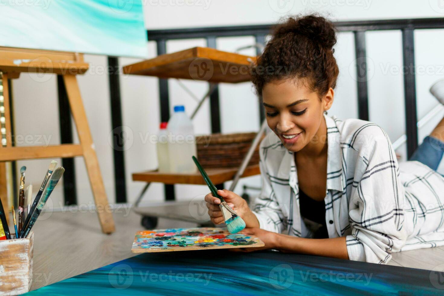 Woman painter lies on the floor  near  canvas and drawing. Artist studio interior. Drawing supplies, oil paints, artist brushes, canvas, frame.  Creative concept. photo