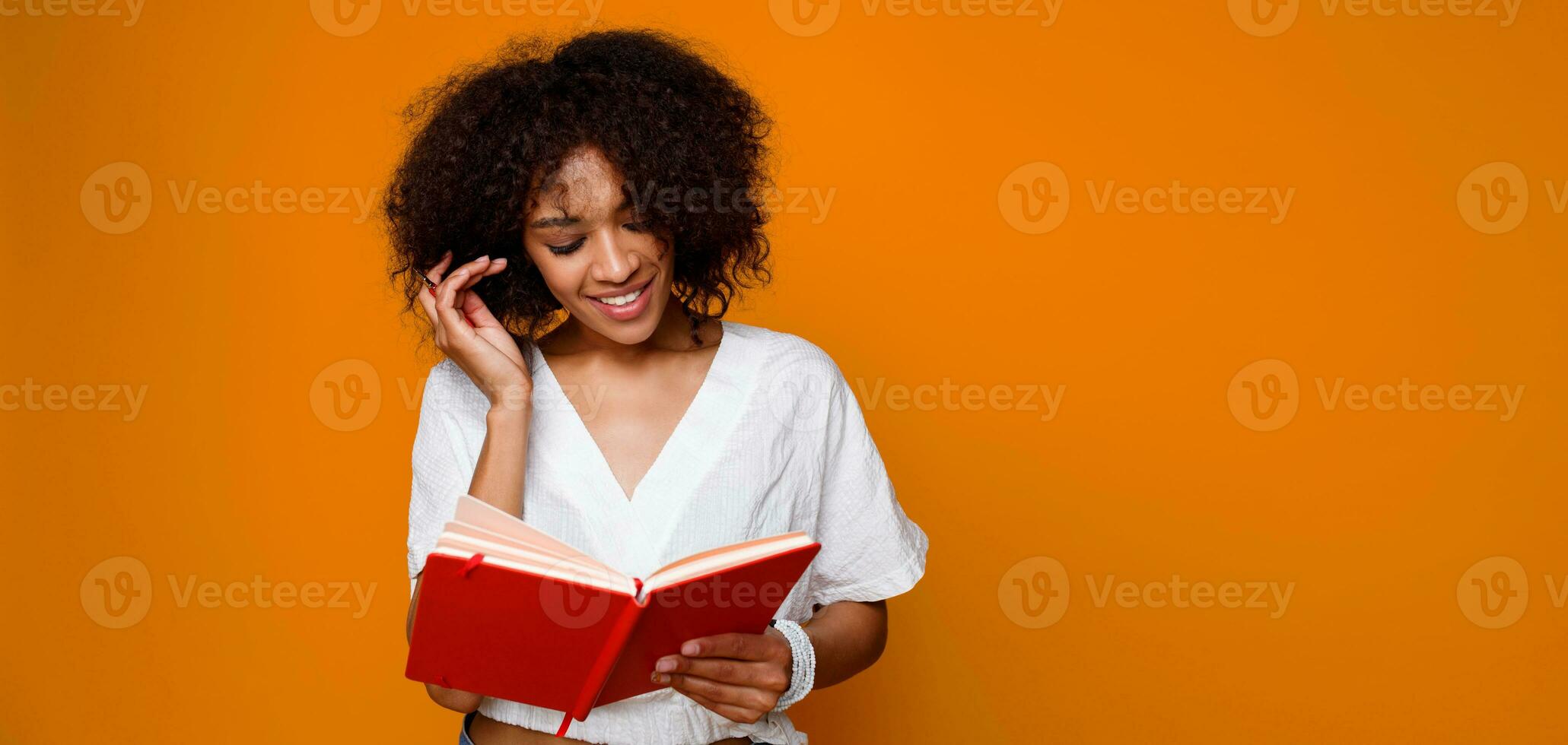 Pensive African student   female  with book poking indoor over orange wall. photo