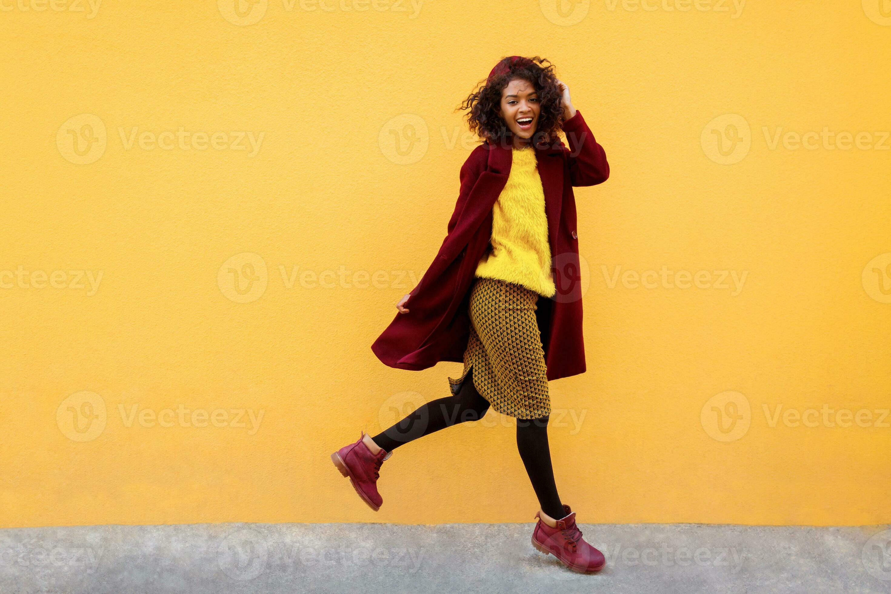 Happy black woman jumping with happy face expression on yellow