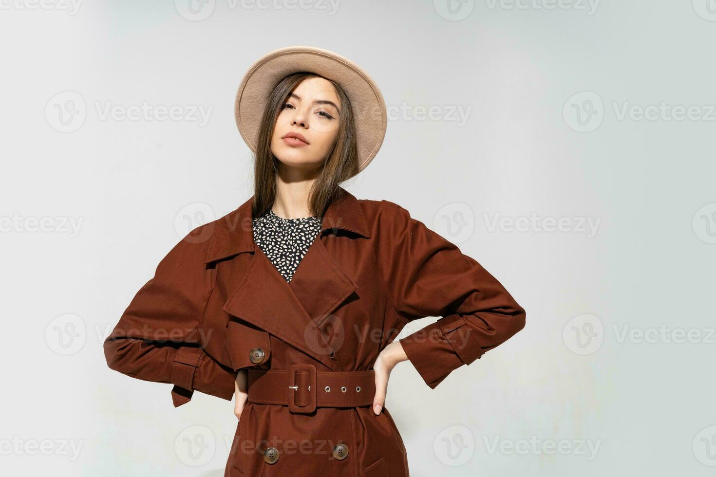 Fashionable woman in brown  coat and  beige hat posing in studio on white background, looking at camera. cold season. Autumn or winter look. photo