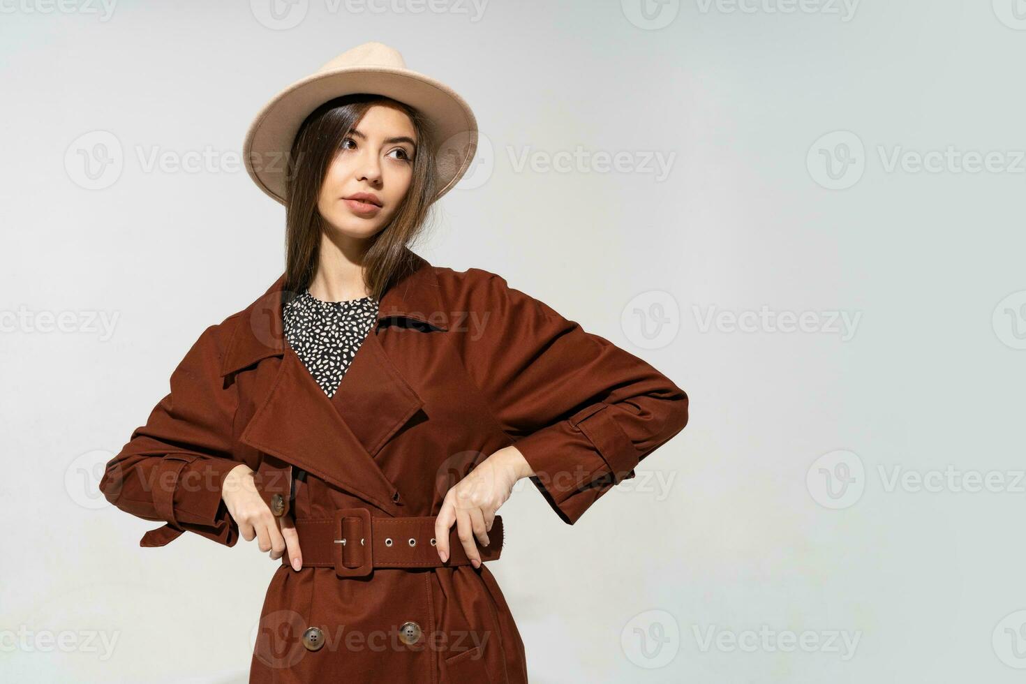 Fashionable woman in brown  coat and  beige hat posing in studio on white background, looking at camera. cold season. Autumn or winter look. photo