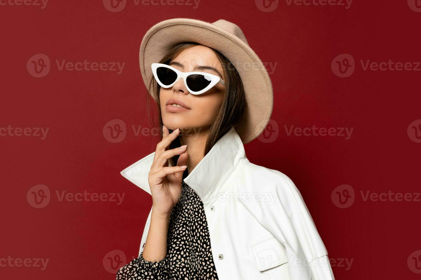 Stylish  woman with perfect skin in beige hat and white jacket posing over red background.  Winter fashion. photo