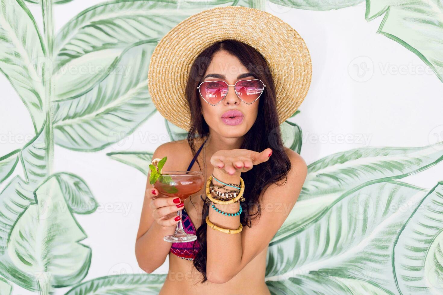 de moda mujer en brillante rosado corazón Gafas de sol bebida Fresco fresa cóctel en playa bar. foto