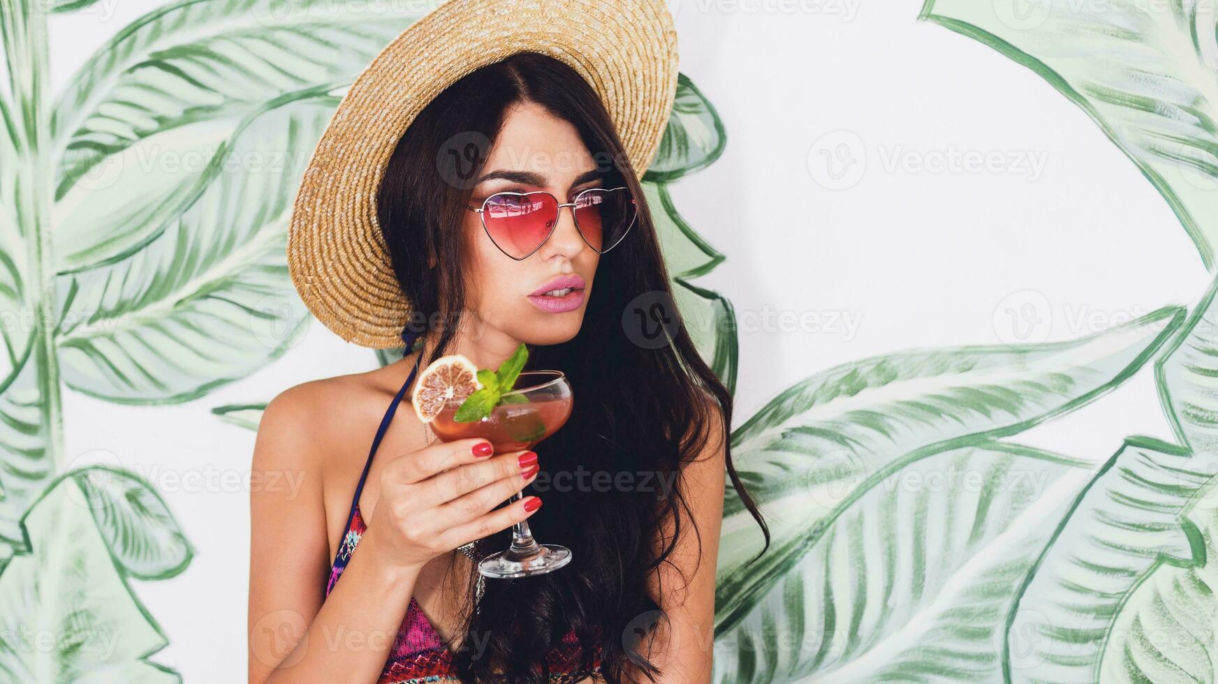 Fashionable woman in bright pink heart sunglasses  drink fresh strawberry cocktail in beach bar. photo