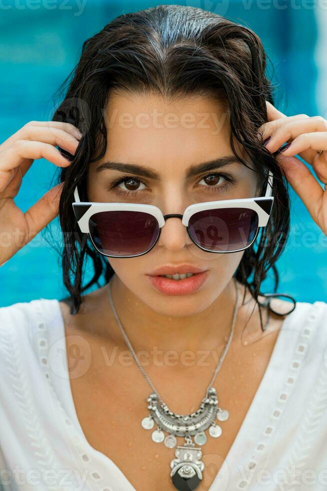 belleza retrato de mujer con Perfecto bronceado piel, en mojado boho atuendo posando en nadando piscina foto