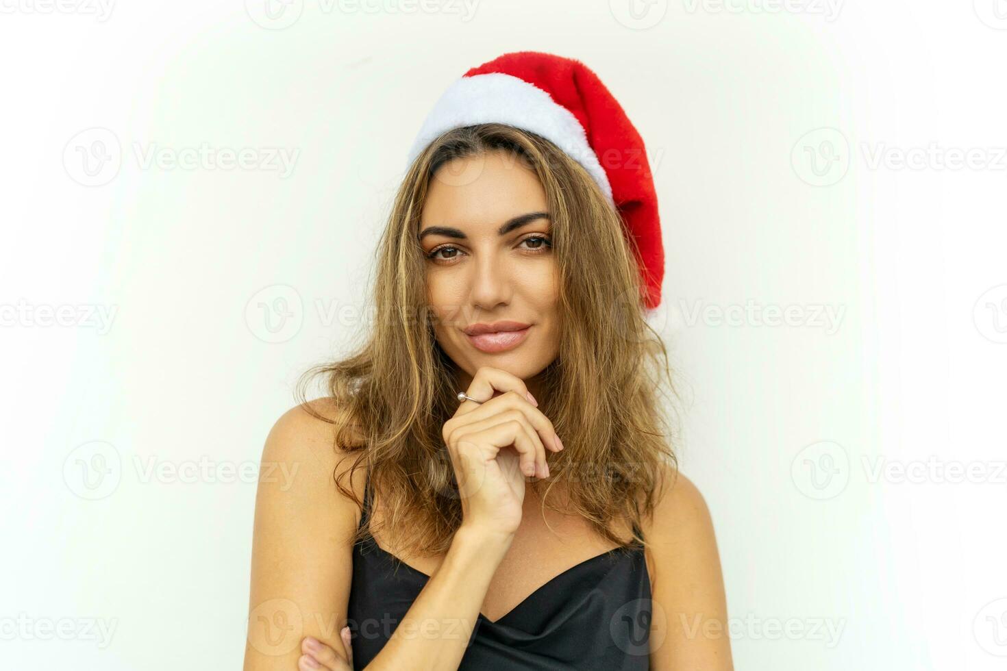 Close up portrait of beautiful brunette woman in  red santa hat posing on white background. Wearing elegant black dress. photo