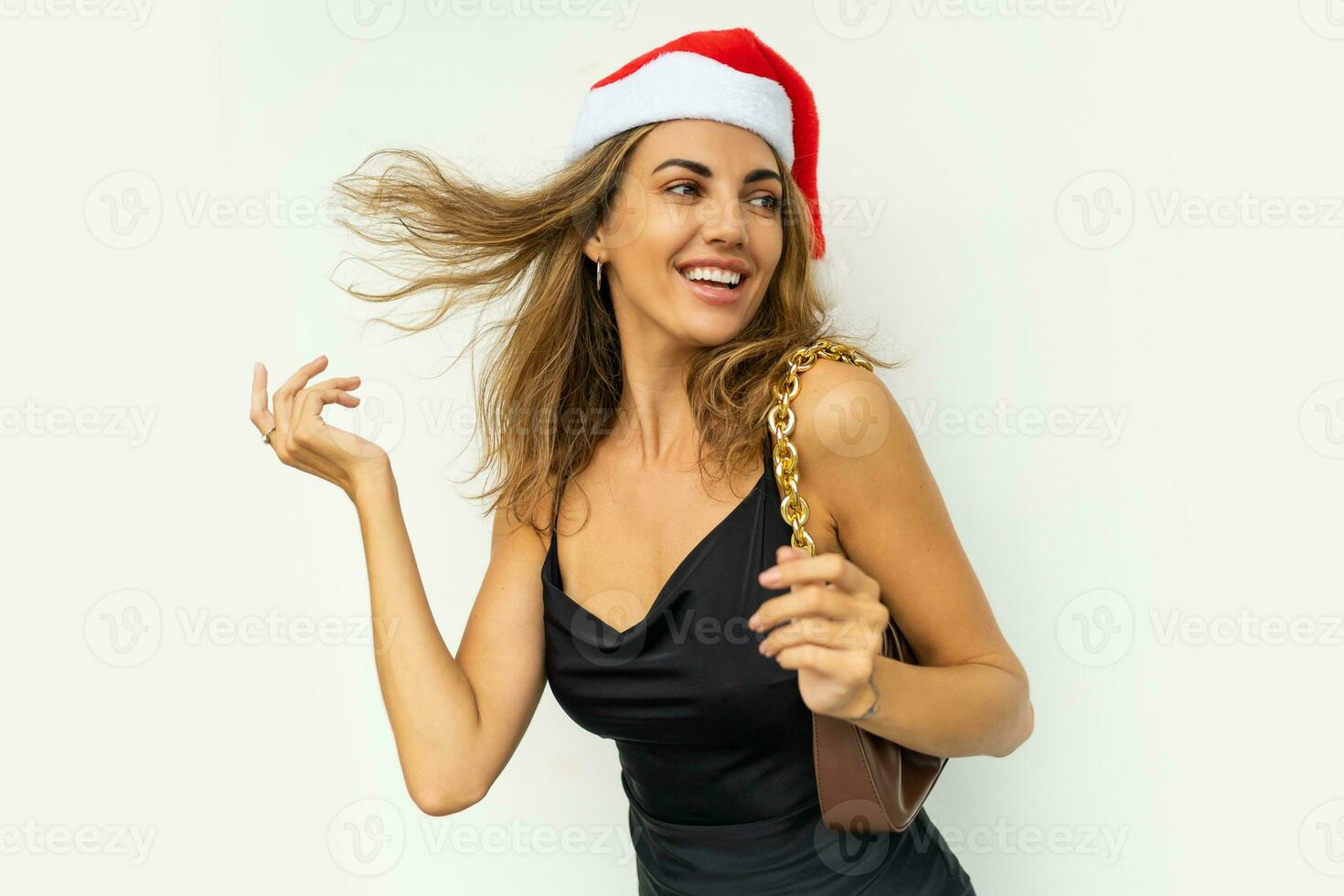 Laughing  celebrating woman in red santa hat and black dress posing on white background. Playing with hairs. photo