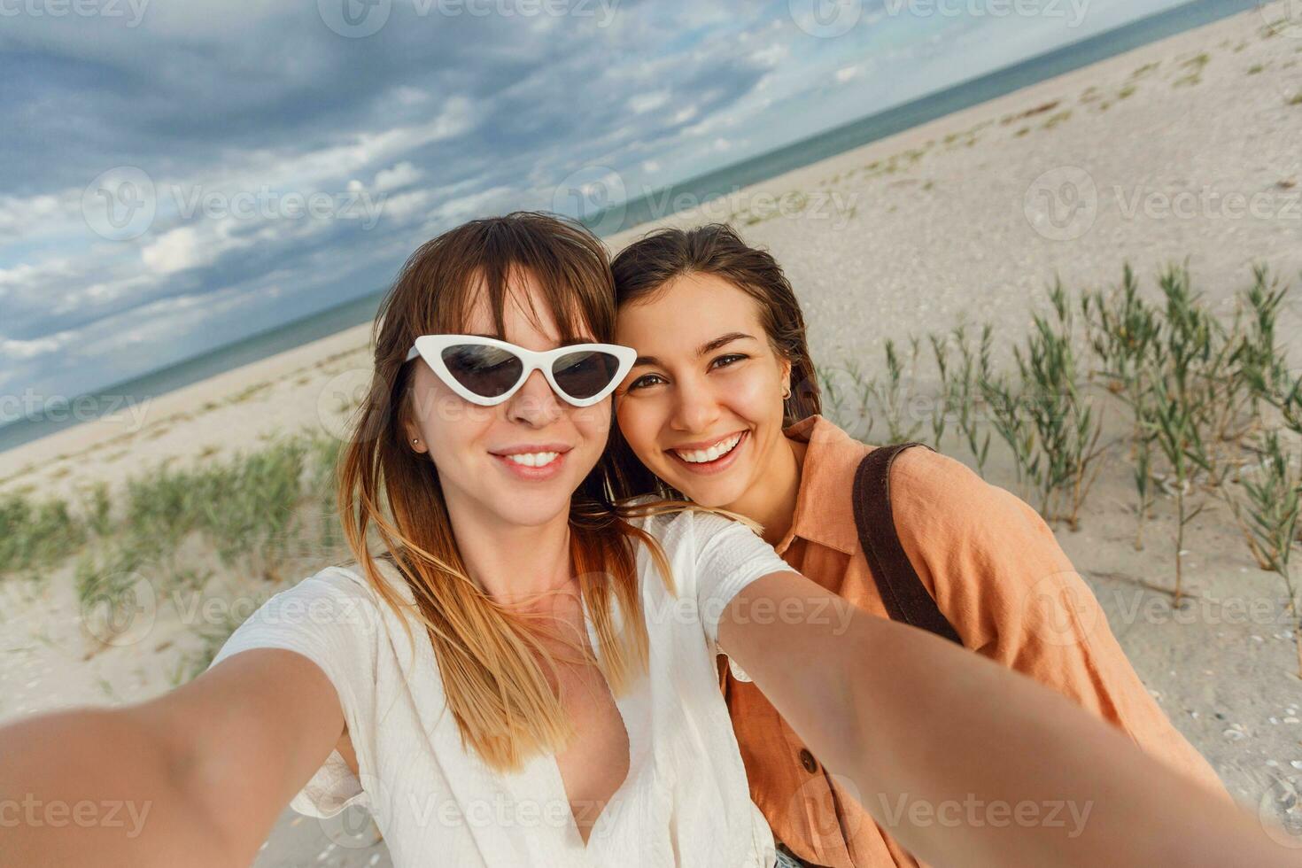 two women smiling and posing for the camera on the beach photo