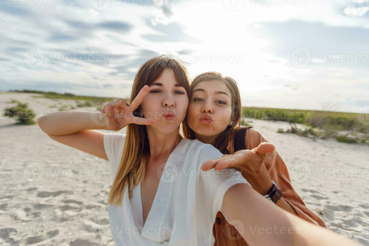 two women smiling and posing for the camera on the beach photo