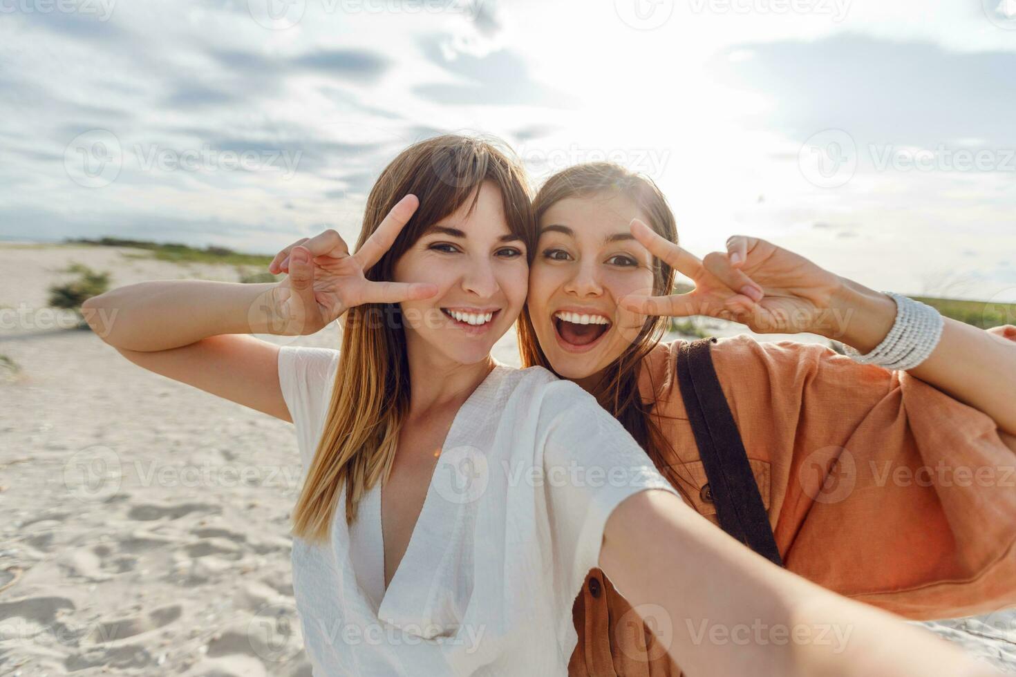 two women smiling and posing for the camera on the beach photo