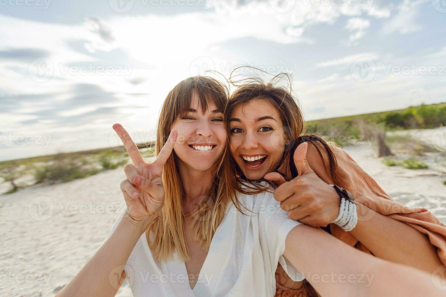 two women smiling and posing for the camera on the beach photo